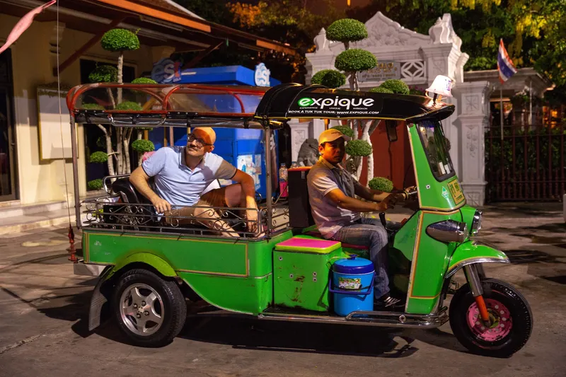 Colourful tuk tuk speeding through Bangkok's illuminated night streets on a tuk tuk tour Bangkok with golden temple spires glowing in the background