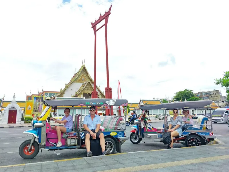 Guide leading tourists in a traditional Thai tuk tuk through Bangkok old city streets lined with temples and golden spires on a tuk tuk tour Bangkok