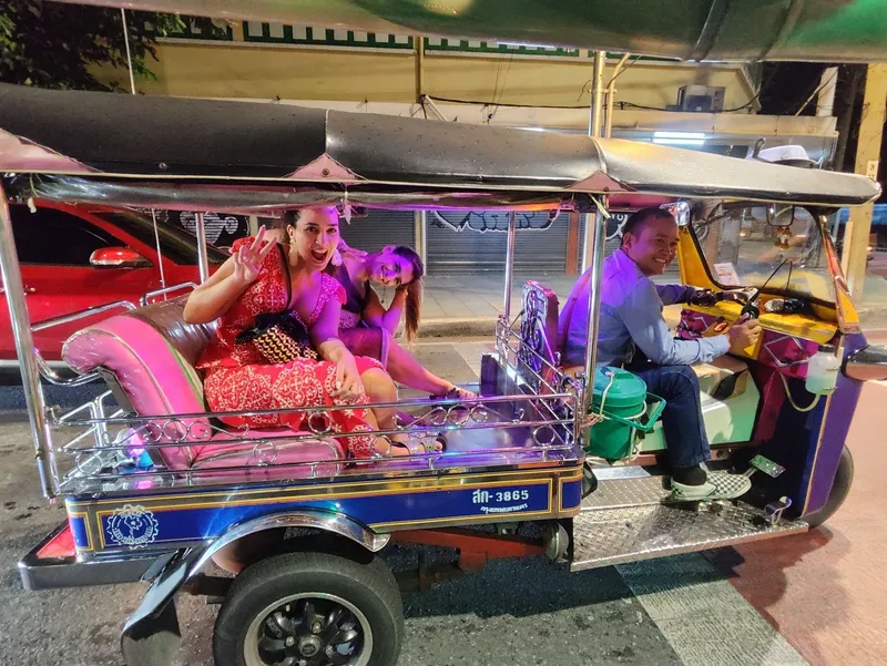 Couple riding a Bangkok tuk tuk at dusk past golden temple spires before a traditional Thai dinner on a tuk tuk tour Bangkok